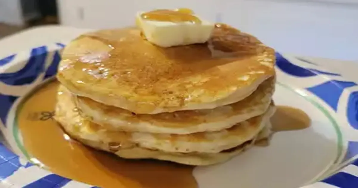 Fluffy homemade pancakes stacked on a plate, topped with a pat of butter and drizzled with golden maple syrup.